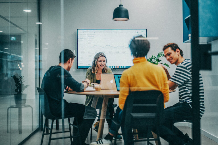 YoungCapital NEXT Trainee Programme Vier junge Menschen sitzen an einem runden Tisch mit ihrem Laptop