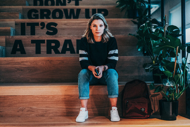 Trainee Programme für Unternehmen Eine Frau sitzt auf einer Trepp und guckt in die Kamera